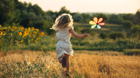 Ein Mädchen mit buntem Windrad rennt über ein Feld