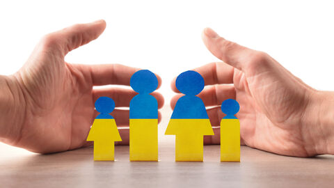 Kleine Holzmännchen, oben blau und unten gelb gestrichen, umgeben von zwei Händen