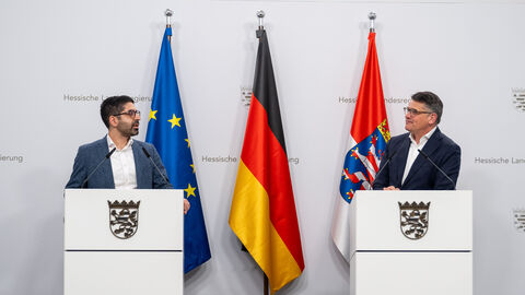 Wirtschaftsminister Kaweh Mansoori und Ministerpräsident Boris Rhein stehen jeweils hinter einem Rednerpult und schauen sich gegenseitig an.