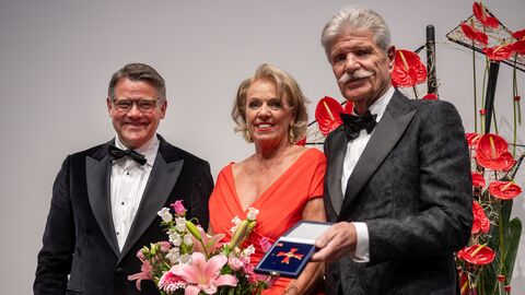 Ministerpräsident Boris Rhein und Sonja und Reinhard Ernst schauen in Kamera. Reinhard Ernst trägt das Bundesverdienstkreuz, Sonja Ernst einen Blumenstrauß