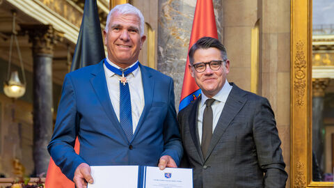 Zwei Personen stehen nebeneinander und halten die Auszeichnung hoch.