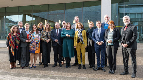 Eine Gruppe steht vor einem Gebäude zum Gruppenfoto aufgestellt.