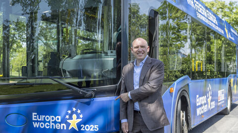 Der hessische Europaminister mit einem Europabus aus Hessen. Manfred Pentz zeigt lachend auf einen blauen Europabus