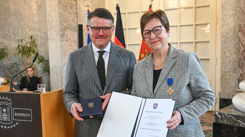 Eine Frau und ein Mann stehen nebeneinander und halten eine Urkunde hoch.