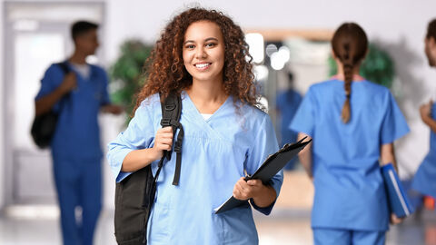 Junge Frau in blauen Krankenhaus-Scrubs lächelt in die Kamera.