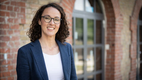 Angela Dorn vor einer Backsteinwand mit großem Fenster
