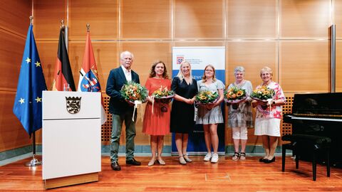Sechs Personen stehen nebeneinander in einem Raum und halten jeweils einen Blumenstrauß in der Hand.