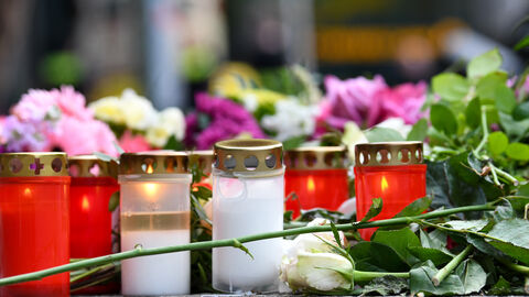 Grabkerzen in rot und weiß stehen auf dem Boden. Um sie herum liegen einzelne Blumen.